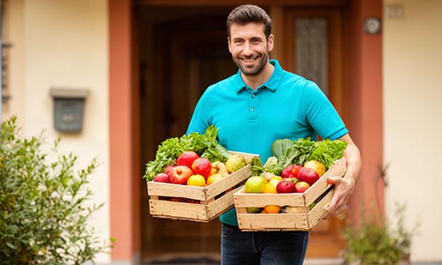 Addetto alla consegna con cassette di frutta fresca davanti a una casa di Faenza